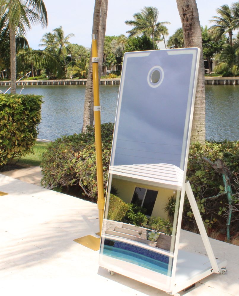 The mirror photo booth on its stand beside the water, palms behind